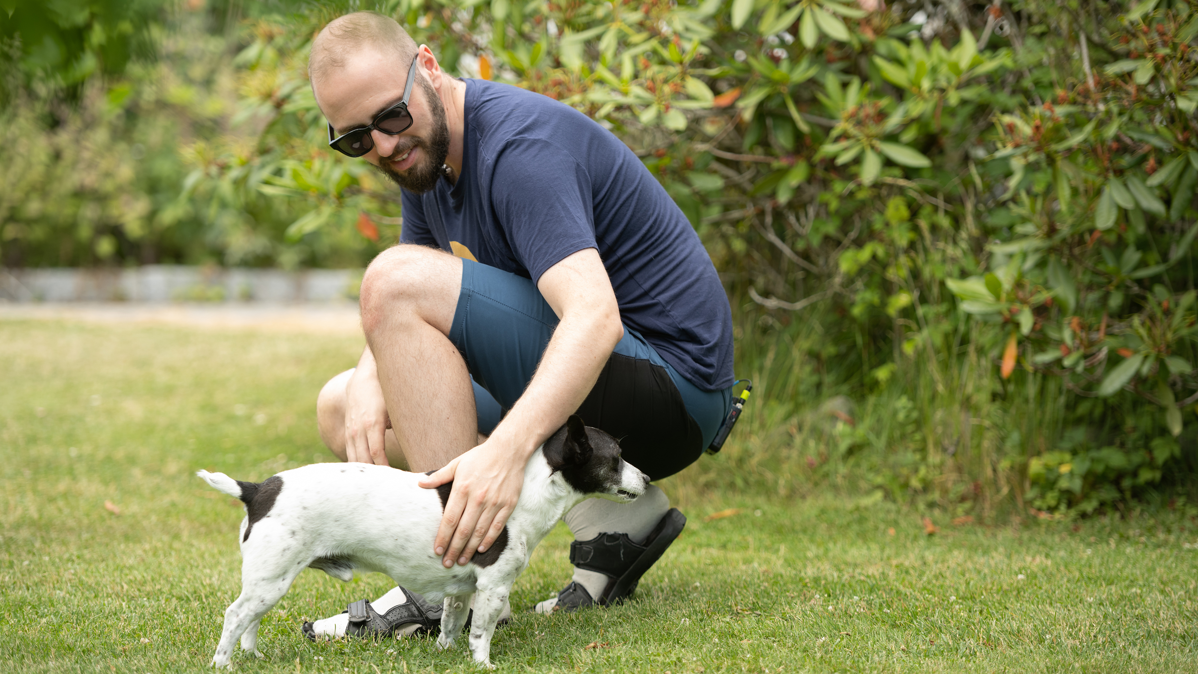Mann bøyer seg ned til hund i hage.