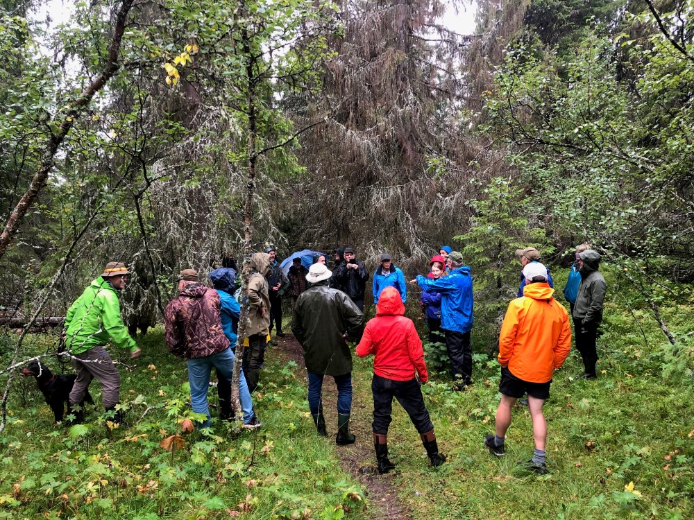 Gruppe mennesker i fargerikt regntøy ute i skogen.