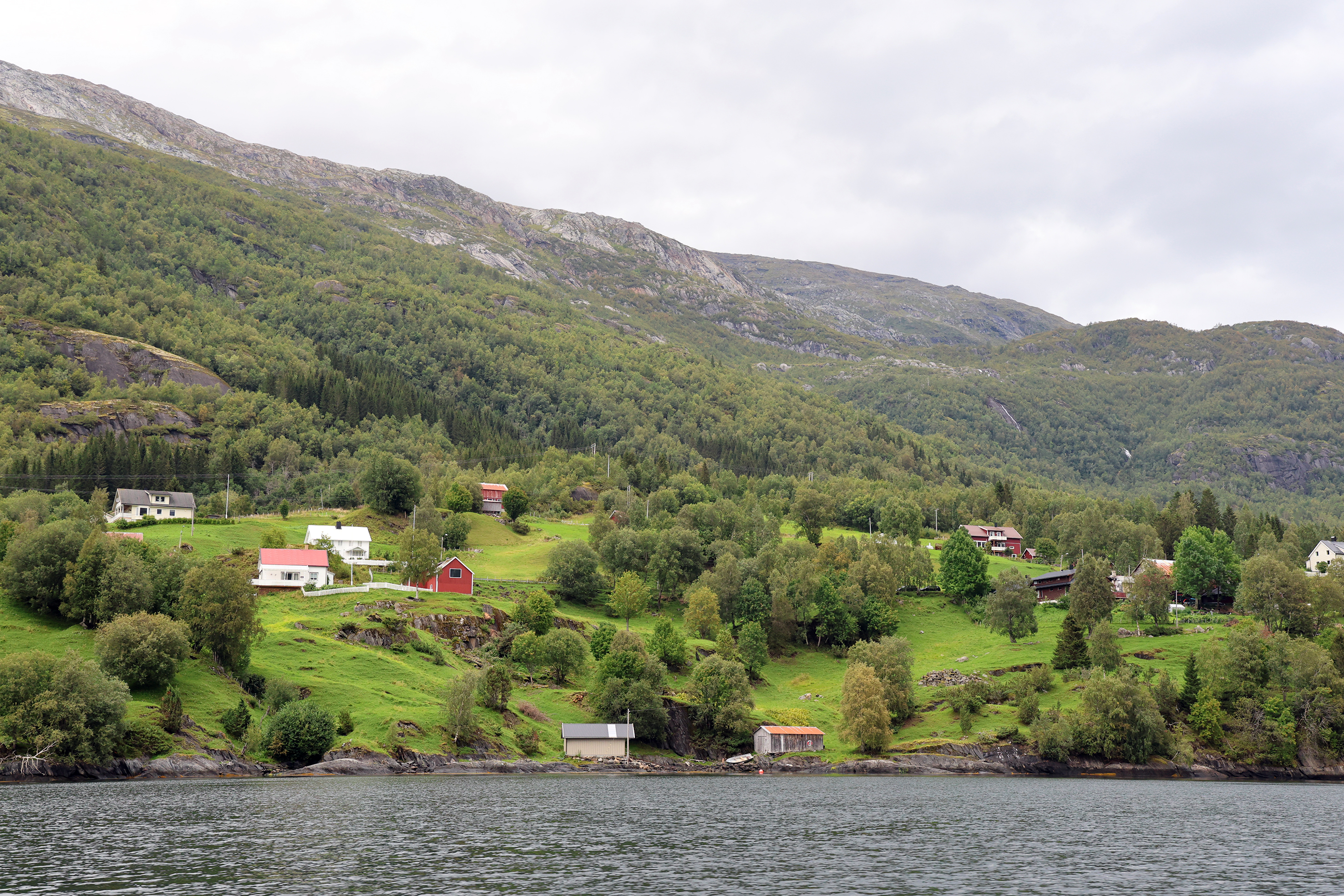landskap med bygninger og grønne beitebakker ned mot en fjord 