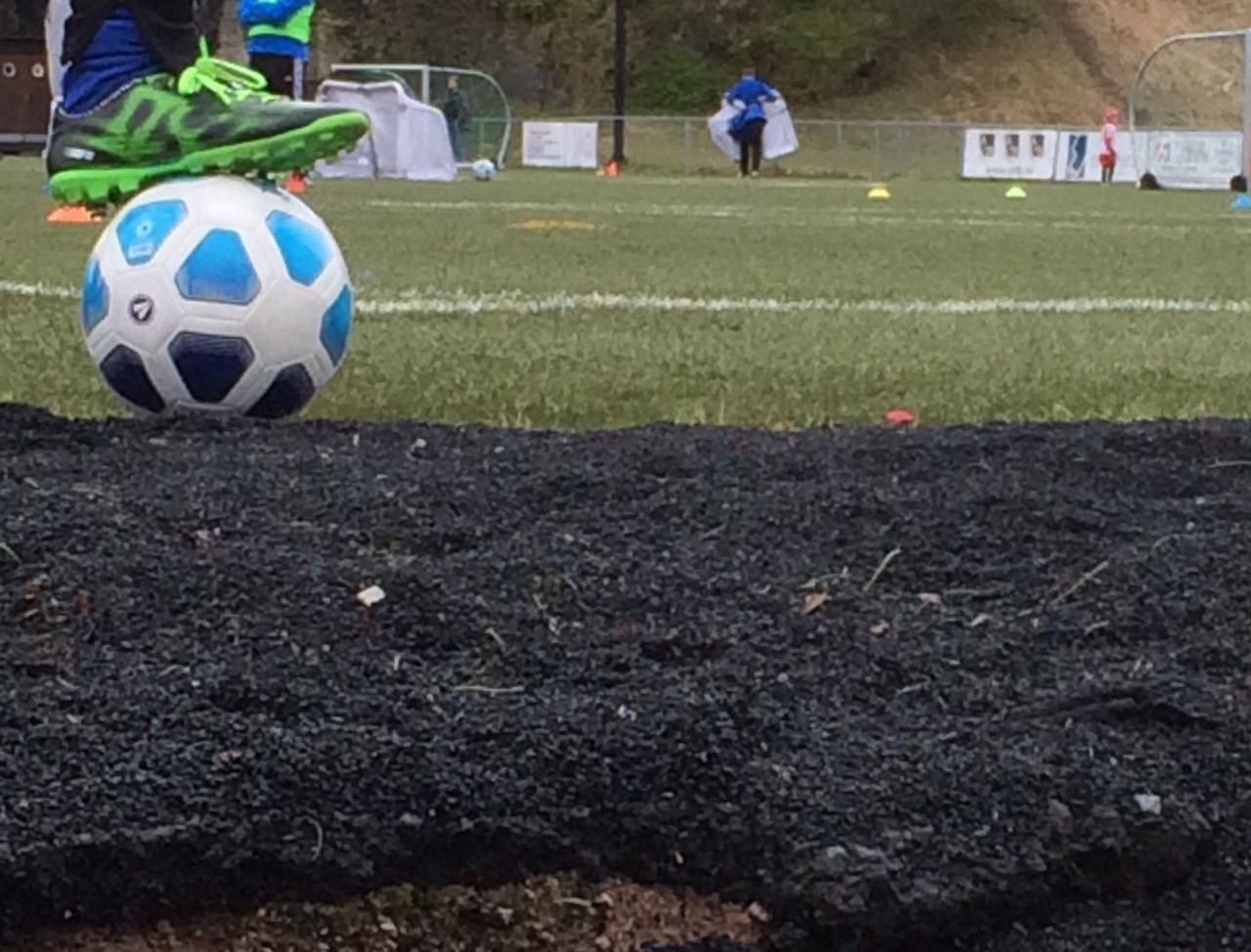 Haug med gummigranulat med en fot på en fotball ved en fotballbane.